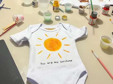 Baby onesie painted with a sun and 'You are my sunshine' at a baby shower